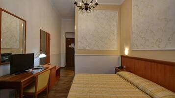 Une chambre d’hôtel comprenant un lit, un bureau avec un ordinateur, une chaise, une télévision et un lustre.