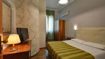 Habitación de hotel con cama, escritorio con lámpara, televisión y ventana con cortinas.