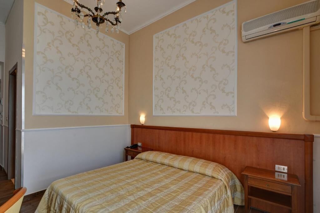Une chambre d’hôtel équipée d’un lit, d’une tête de lit en bois, d’un climatiseur fixé au mur et de panneaux décoratifs.