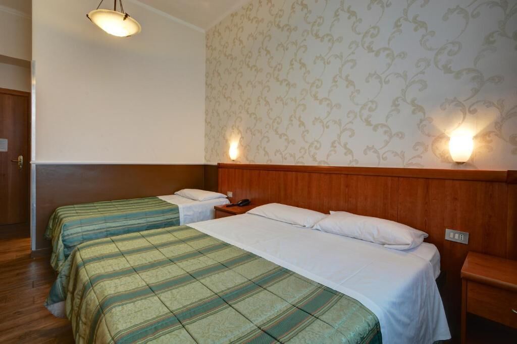 Une chambre d’hôtel avec deux lits, des têtes de lit en bois, un papier peint à motifs et des lampes fixées au mur.