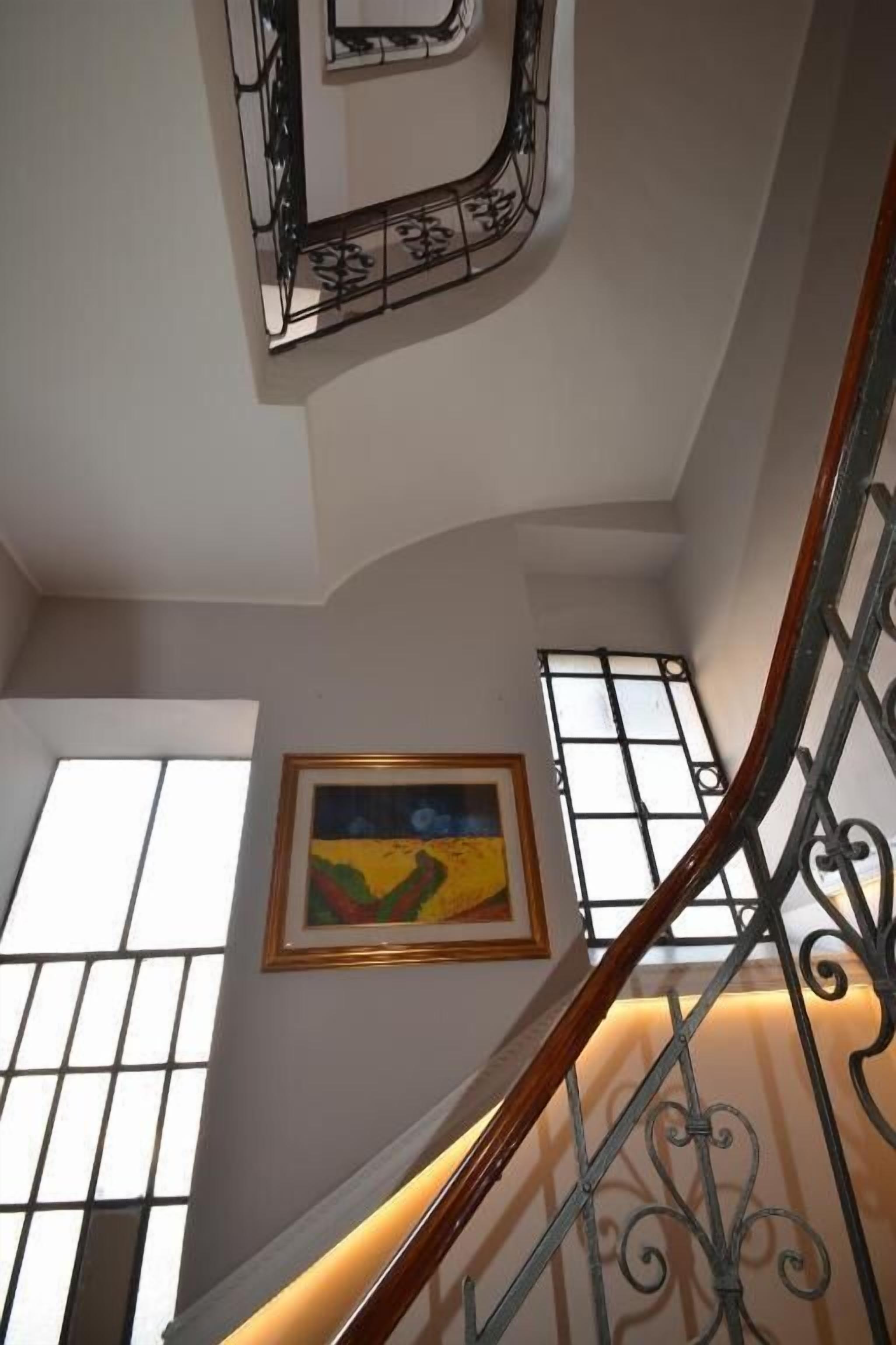A staircase with ornate metal railings and a wooden handrail, leading to a landing with a framed painting.