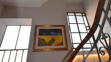 A staircase with ornate metal railings and a wooden handrail, leading to a landing with a framed painting.