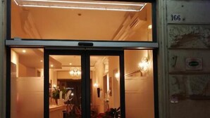 A hotel entrance with a glass door, a reception desk, and a seating area with red chairs. - HOTEL UNIVERSO (Turin)