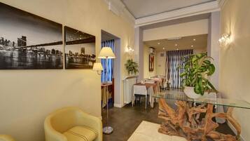 Un hall d’hôtel moderne avec une table basse en verre, un fauteuil jaune et un grand tableau représentant un paysage urbain.