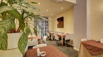 Uma sala de jantar com mesas e cadeiras, uma planta grande em vaso e uma parede com padrão listrado vertical.