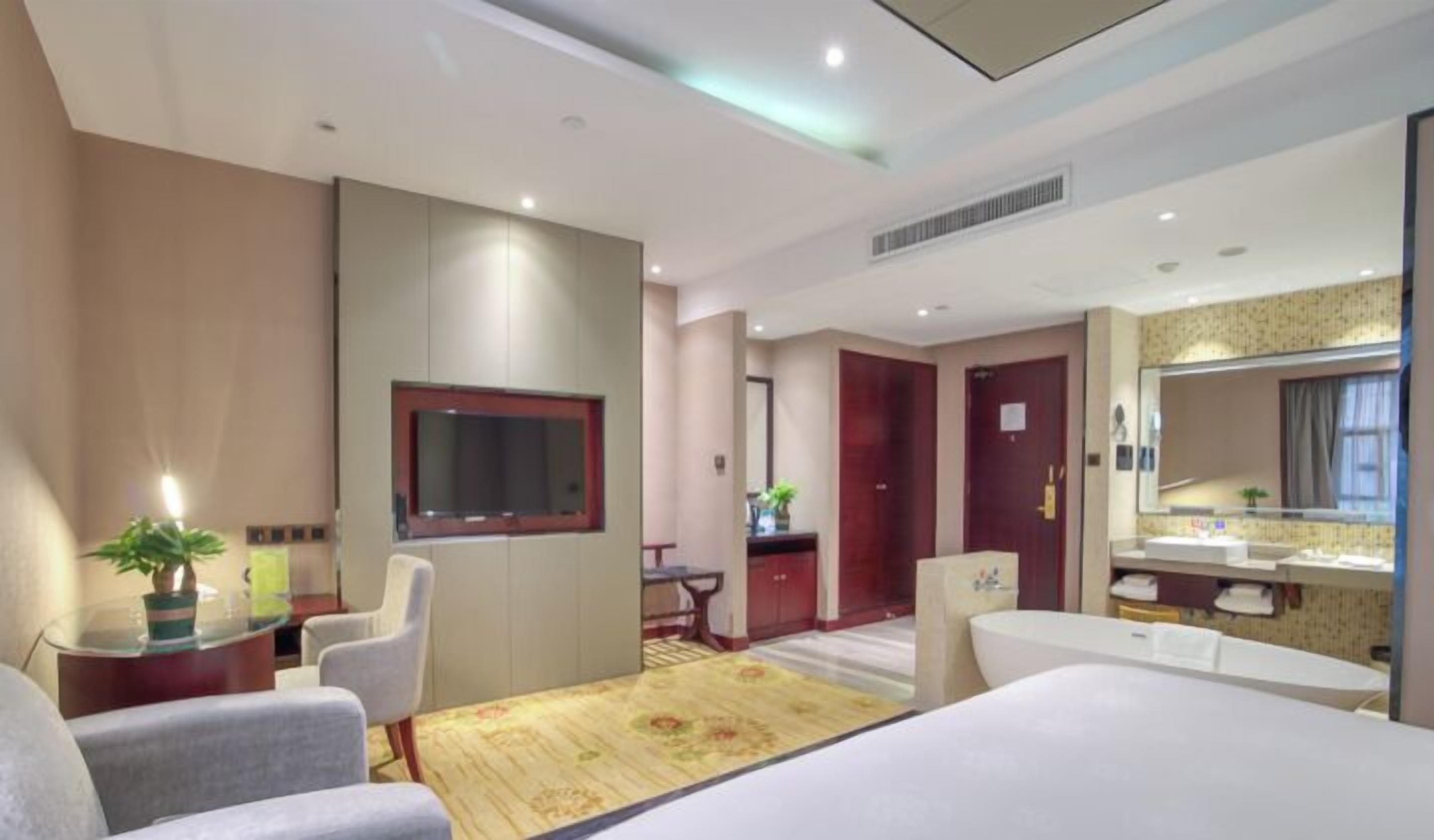 Habitació d'hotel amb llit, escriptori, cadira, televisió, bany amb rentaplat i mirall, i terra amb moqueta.