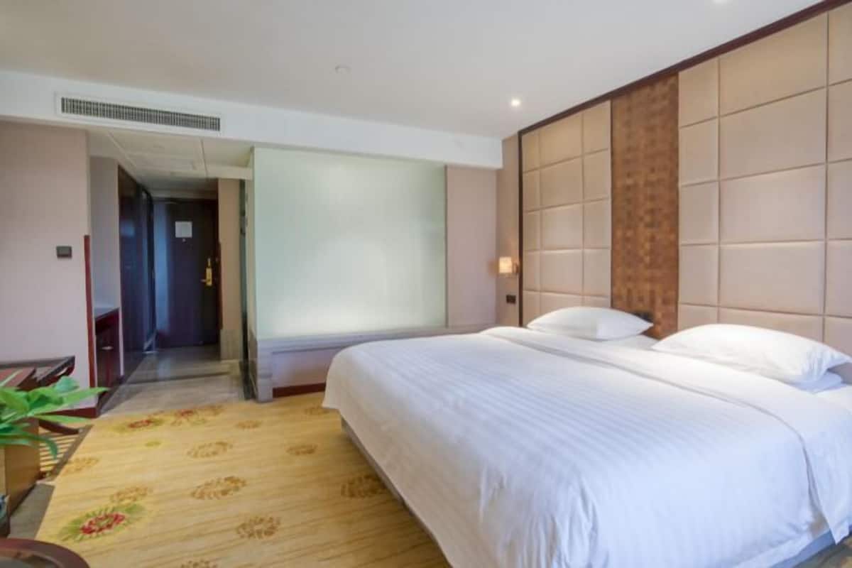 Une chambre d’hôtel avec un grand lit, une tête de lit en bois, une table de chevet avec un téléphone et un sol recouvert de moquette.