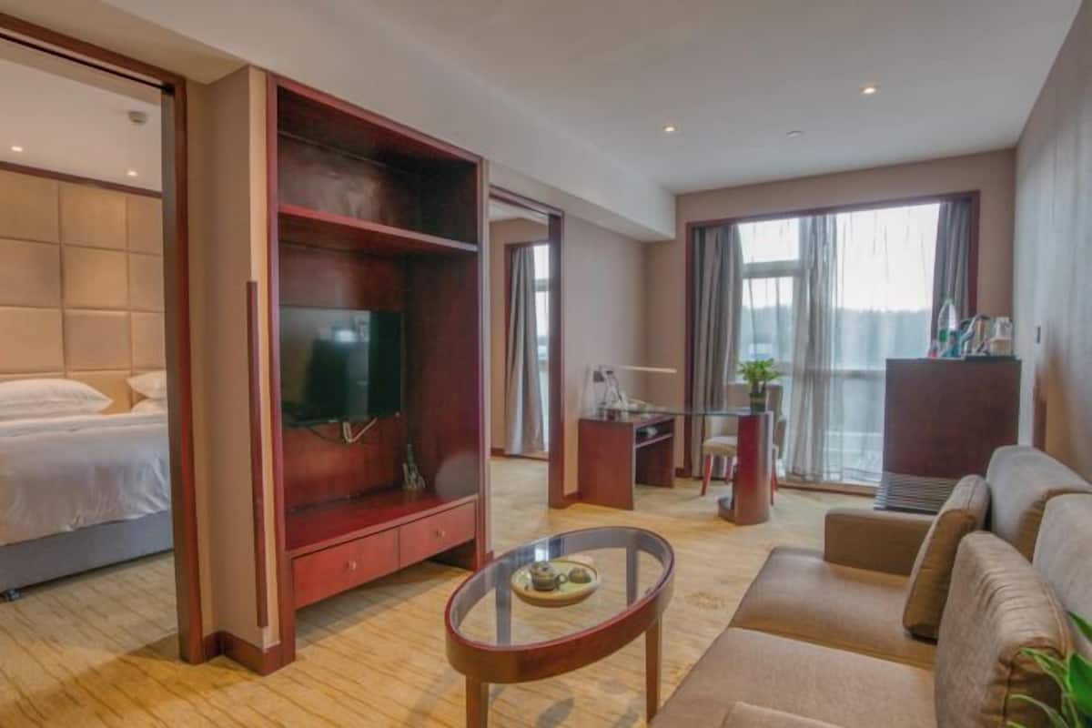 Une chambre d’hôtel comprenant un lit, une télévision, un bureau avec une chaise, un canapé et une table basse en verre.