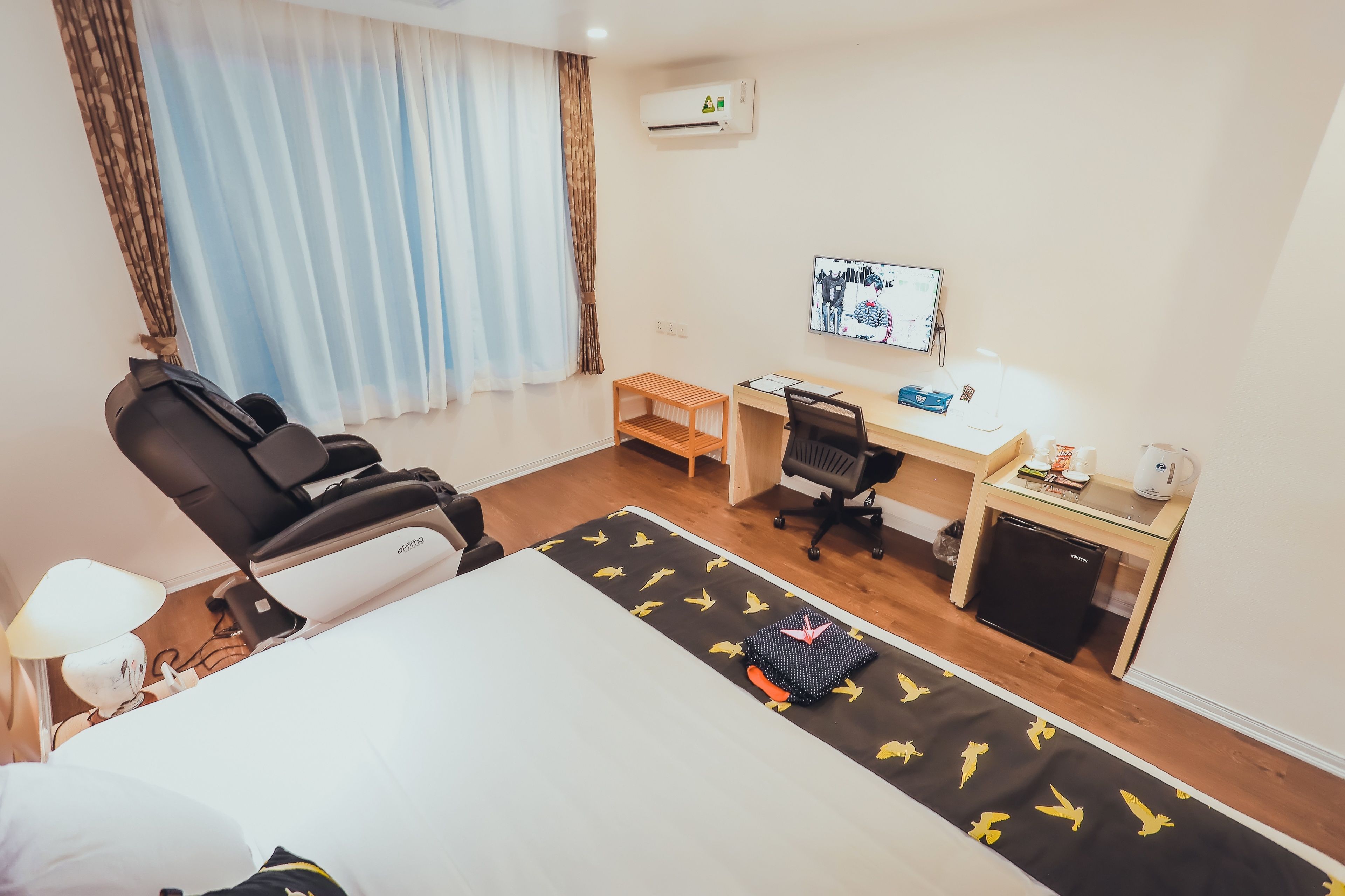 Une chambre d’hôtel avec un lit, un bureau, une chaise, une petite table, un téléviseur et une fenêtre avec des rideaux.