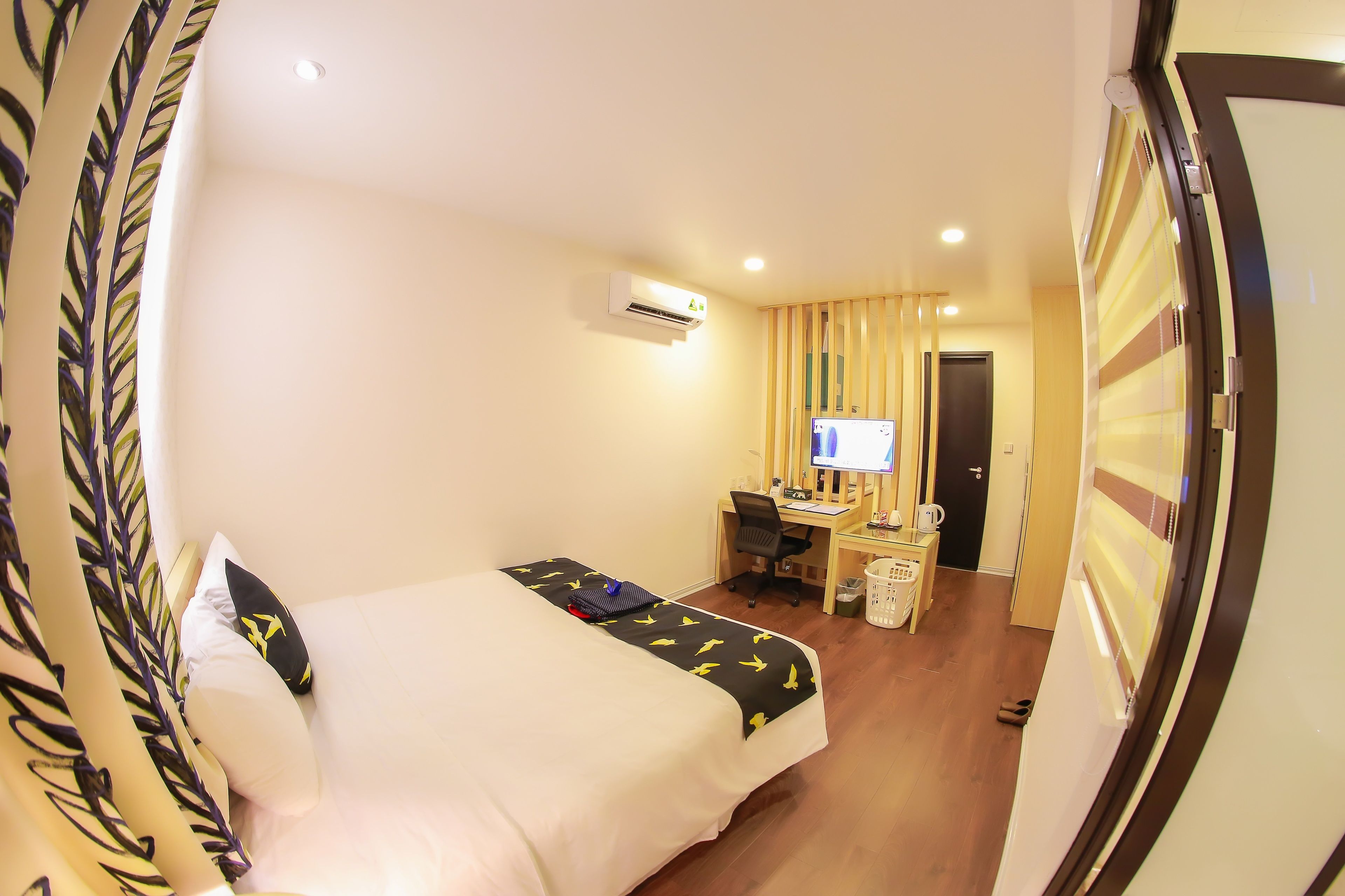 A hotel room with a bed, a desk, a chair, an air conditioning unit, and a television.