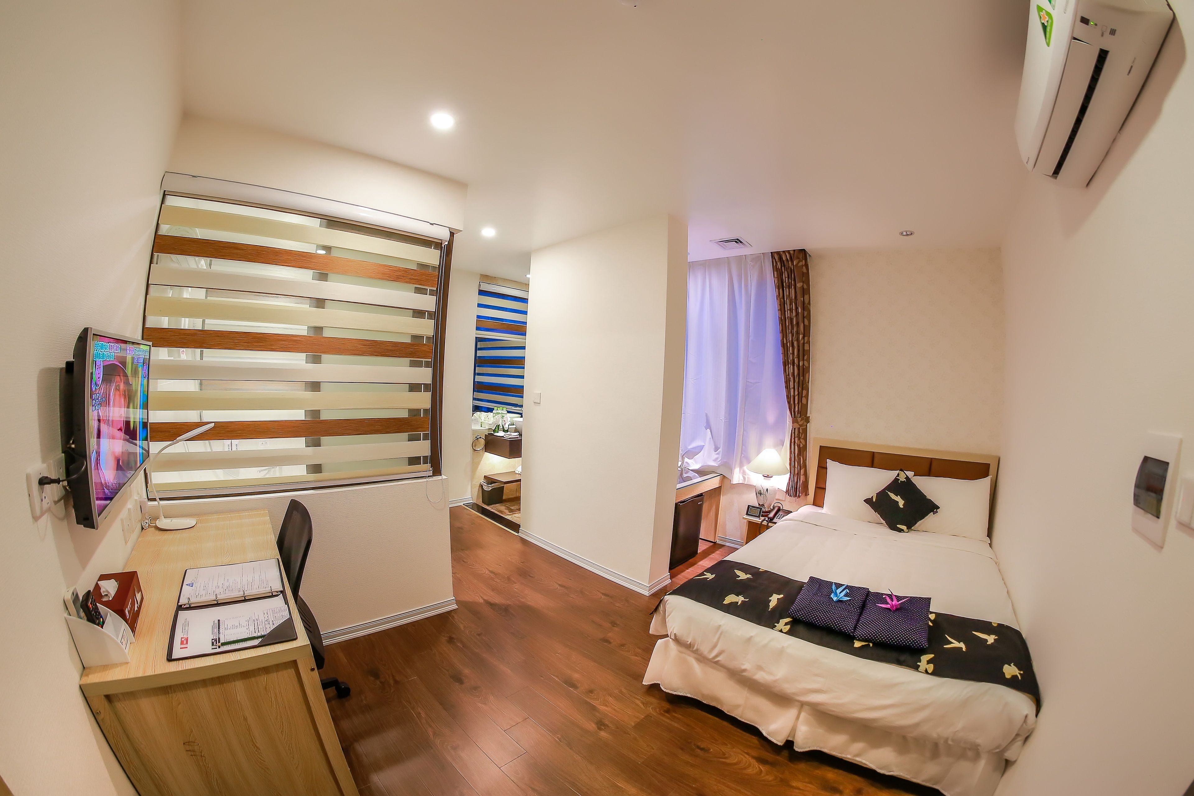 A hotel room with a desk, a bed, and a TV.