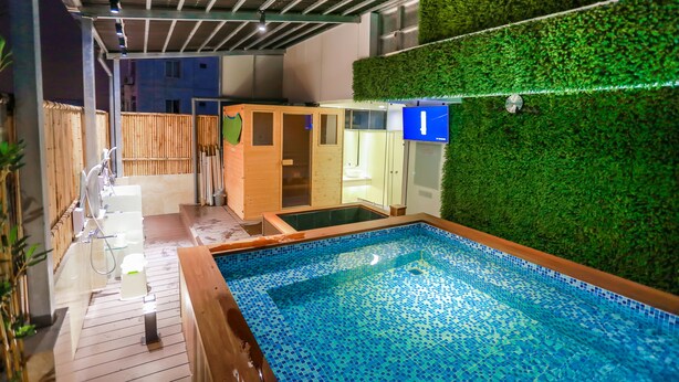 Una piscina con piso de baldosas, cubierta de madera y pared verde con jardín vertical.