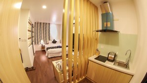 Habitación de hotel compacta con kitchenette, una cama con cabecera estampada y vistas a través de un separador de madera.