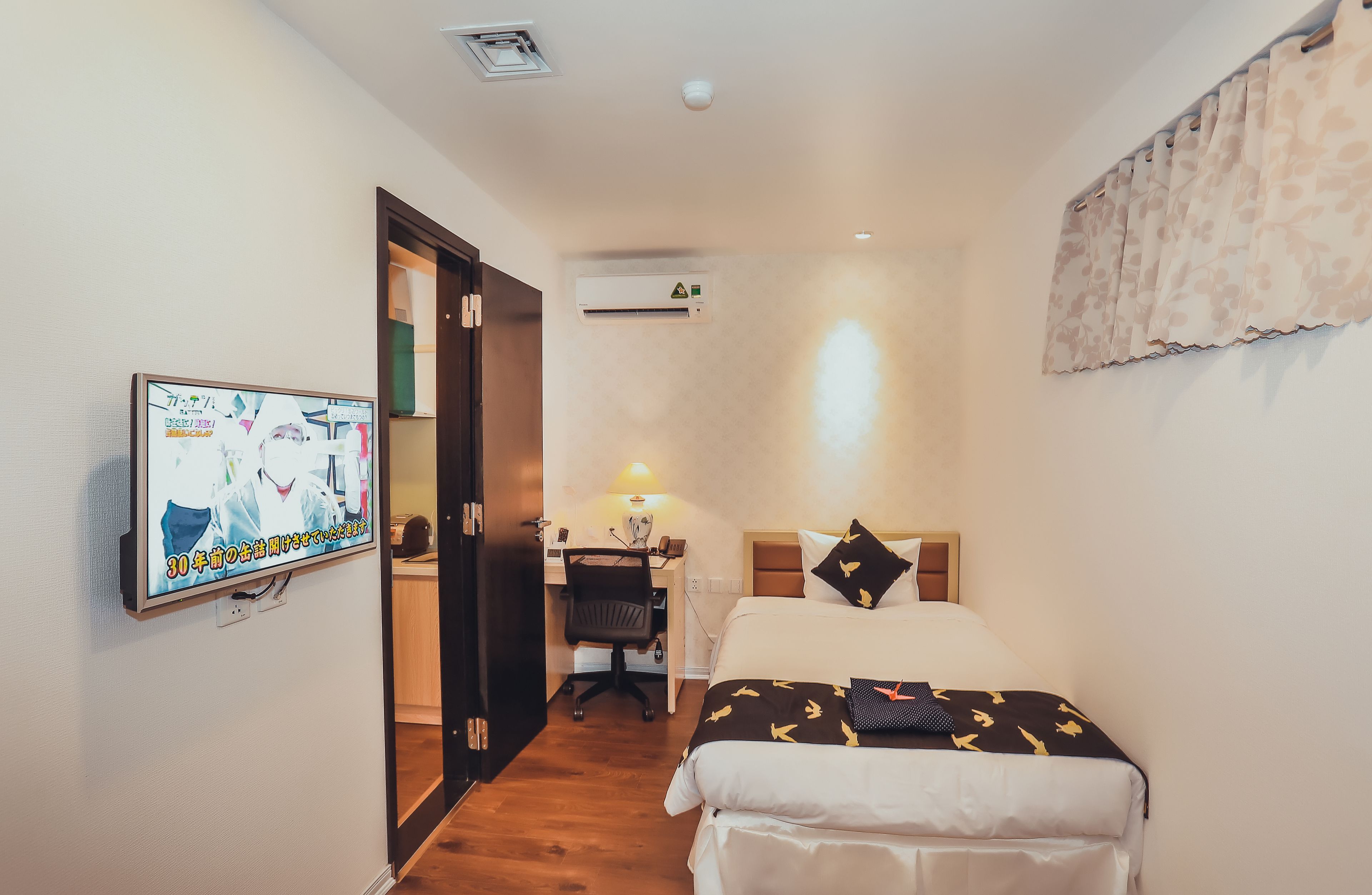 Ein Hotelzimmer mit Bett, Schreibtisch mit Stuhl, Wandfernseher und Klimaanlage.