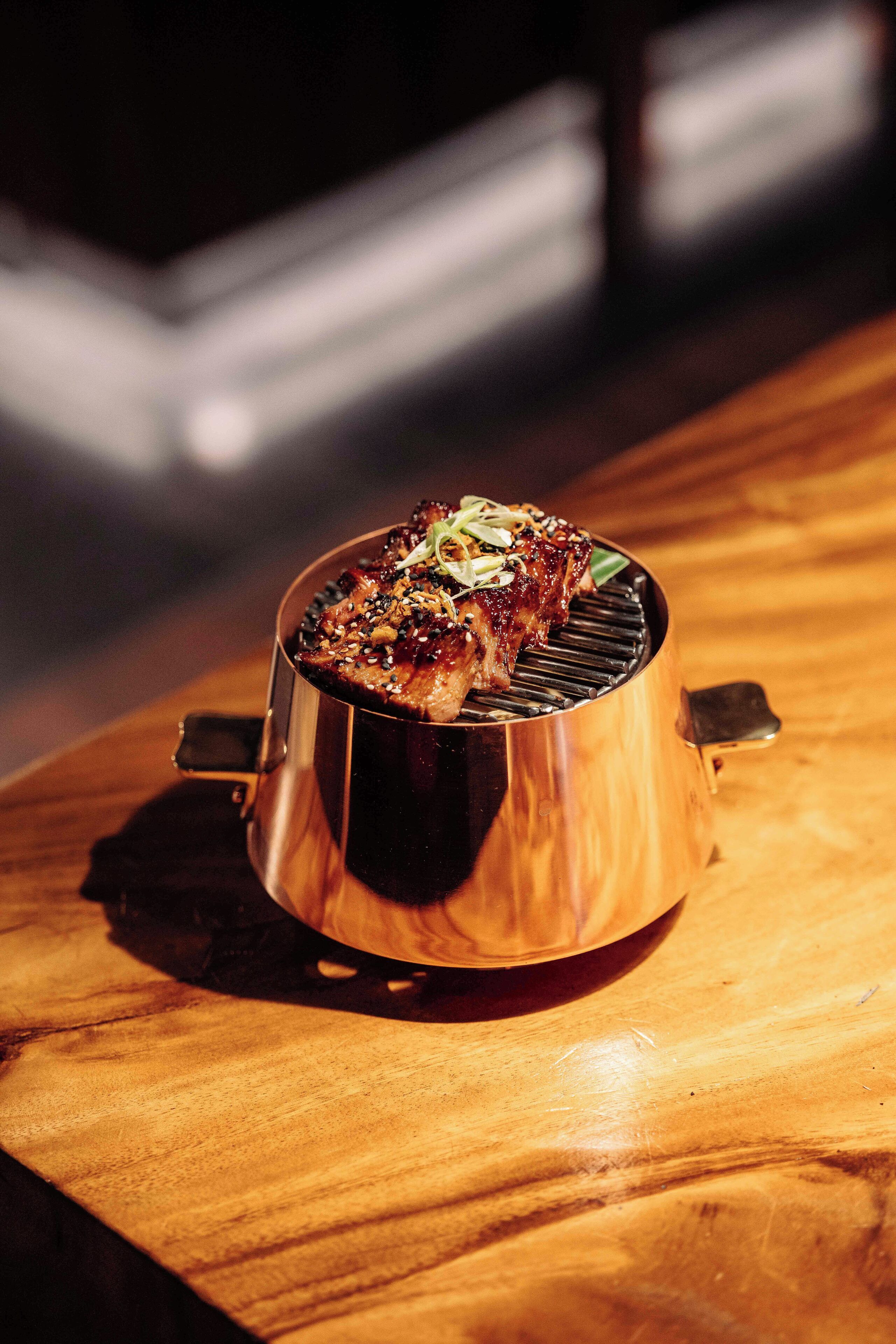 A stainless steel portable grill with a lid, placed on a wooden table.