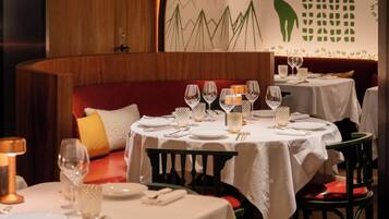 Un ristorante con tavoli rotondi, tovaglie bianche e sedute imbottite rosse.
