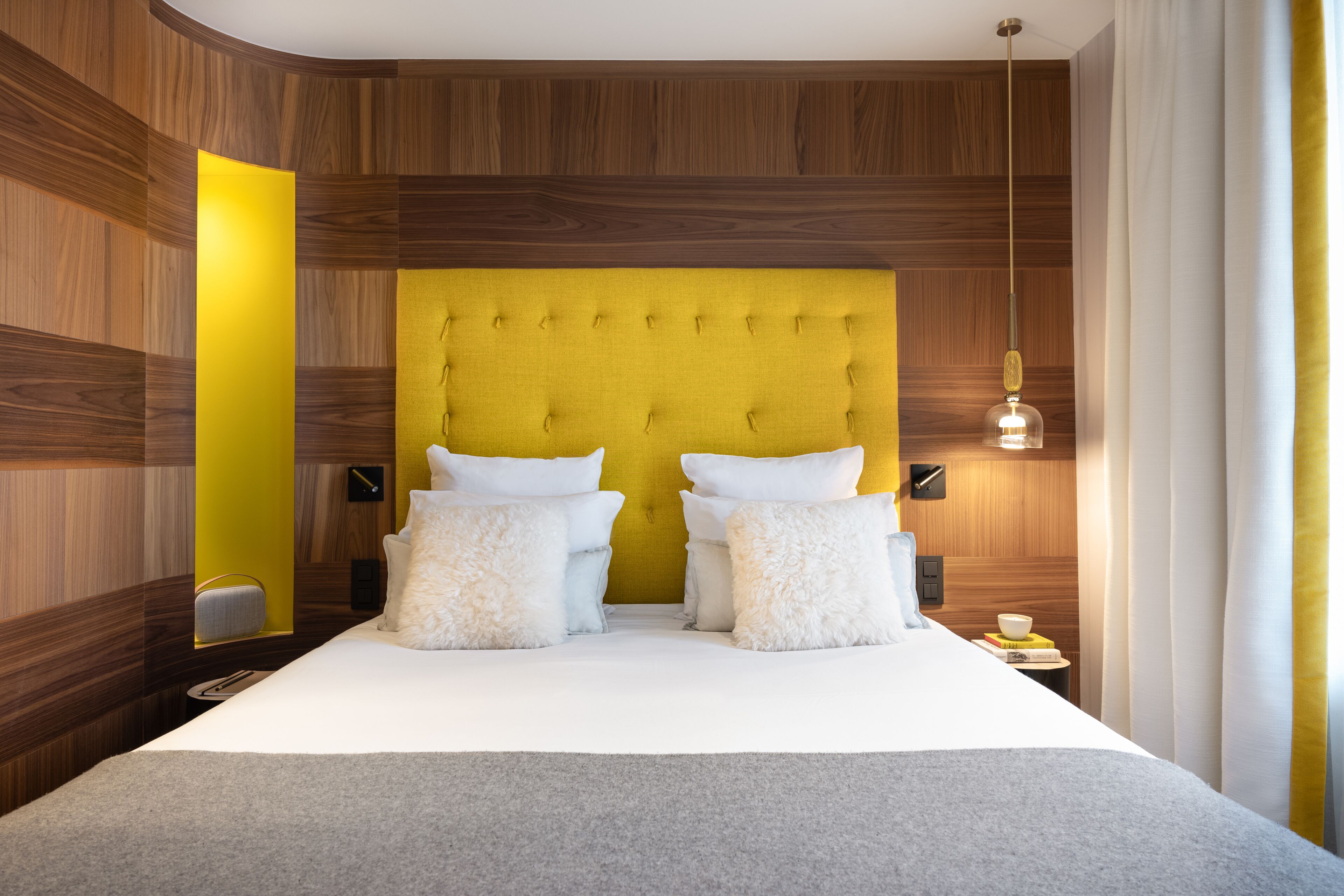 Een moderne hotelkamer met een groot bed, houten paneelwanden en een felgele accentmuur.