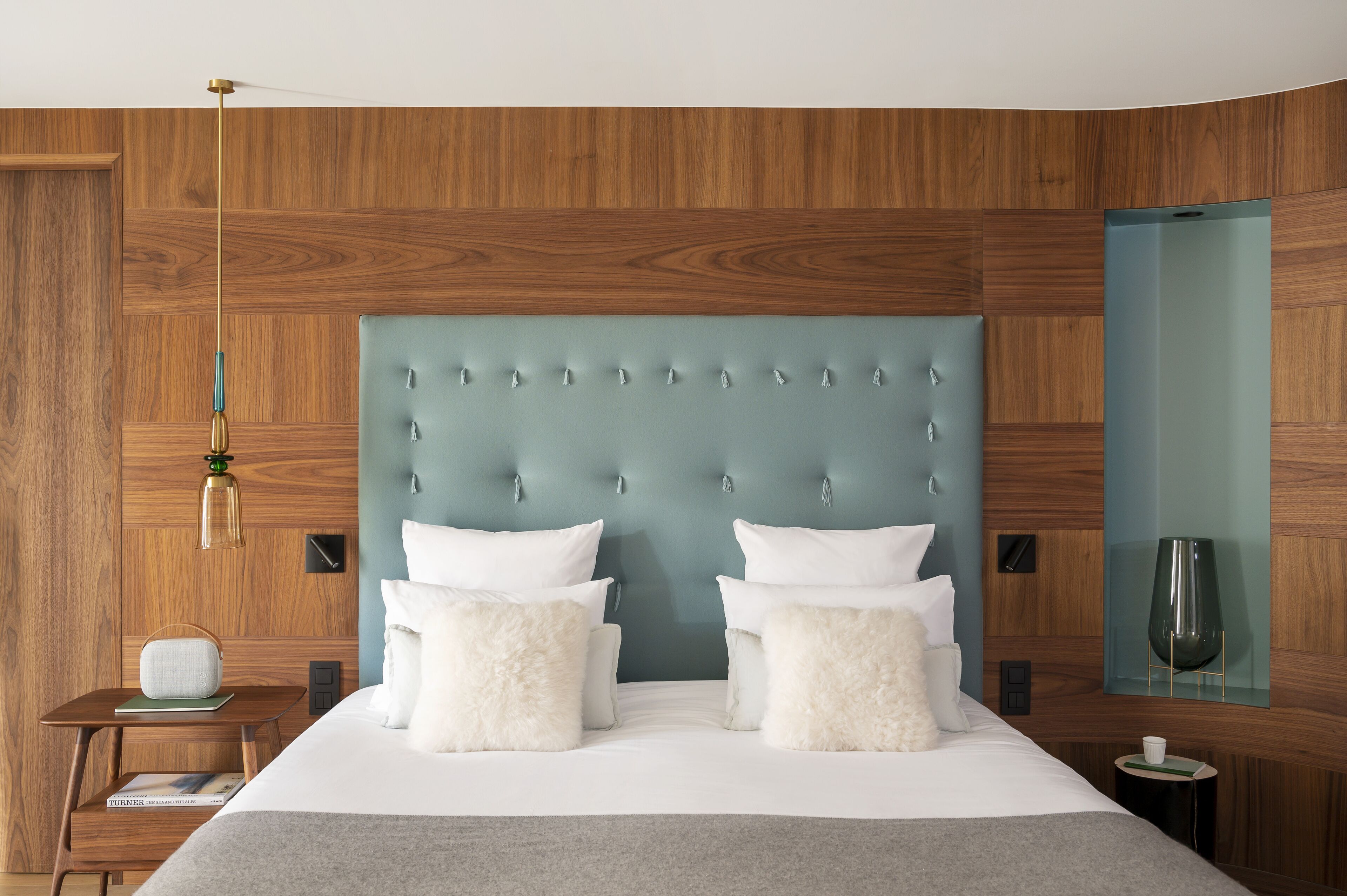 A modern bedroom with a tufted headboard, a bedside table with a lamp, and a nightstand with a book and a cup.
