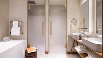 A modern bathroom with a bathtub, two sinks, a shower, and a vanity with a mirror.