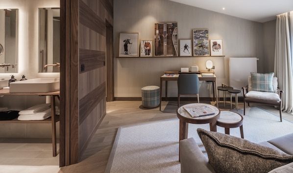 A modern hotel room with a wooden floor, a desk with a chair, a sofa, a small table with a newspaper, and a large mirror. - Coeur de Megève (Megeve)
