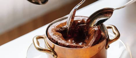 A person stirring a hot chocolate in a copper pot on a white table.