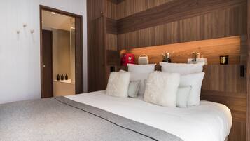 A modern hotel room with a wooden headboard, a large bed with white bedding, a grey throw blanket, and a mirror on the wall.