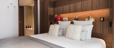 Une chambre d’hôtel moderne avec une tête de lit en bois, un grand lit avec une literie blanche, un plaid gris et un miroir au mur.