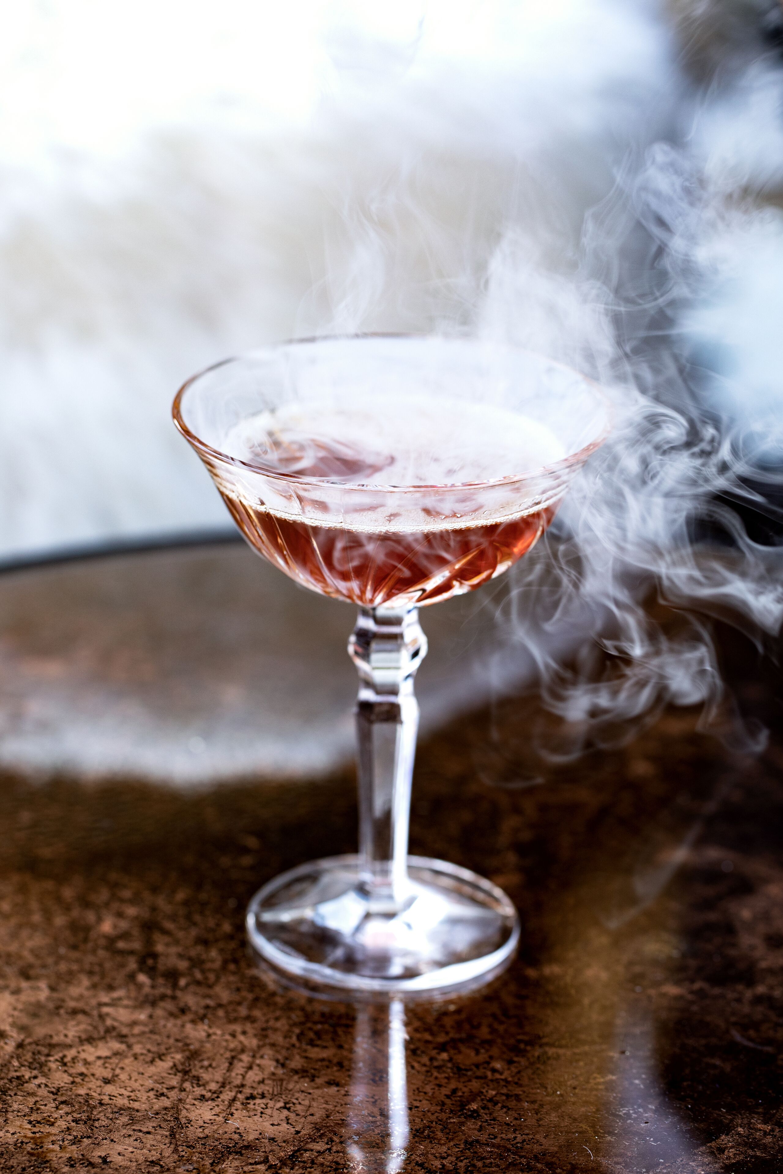 A cocktail glass with a smoky effect, placed on a textured surface.