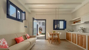 Un salon moderne avec un canapé beige, une table à manger avec des chaises et un coin cuisine doté de meubles en bois et d’un plan de travail.