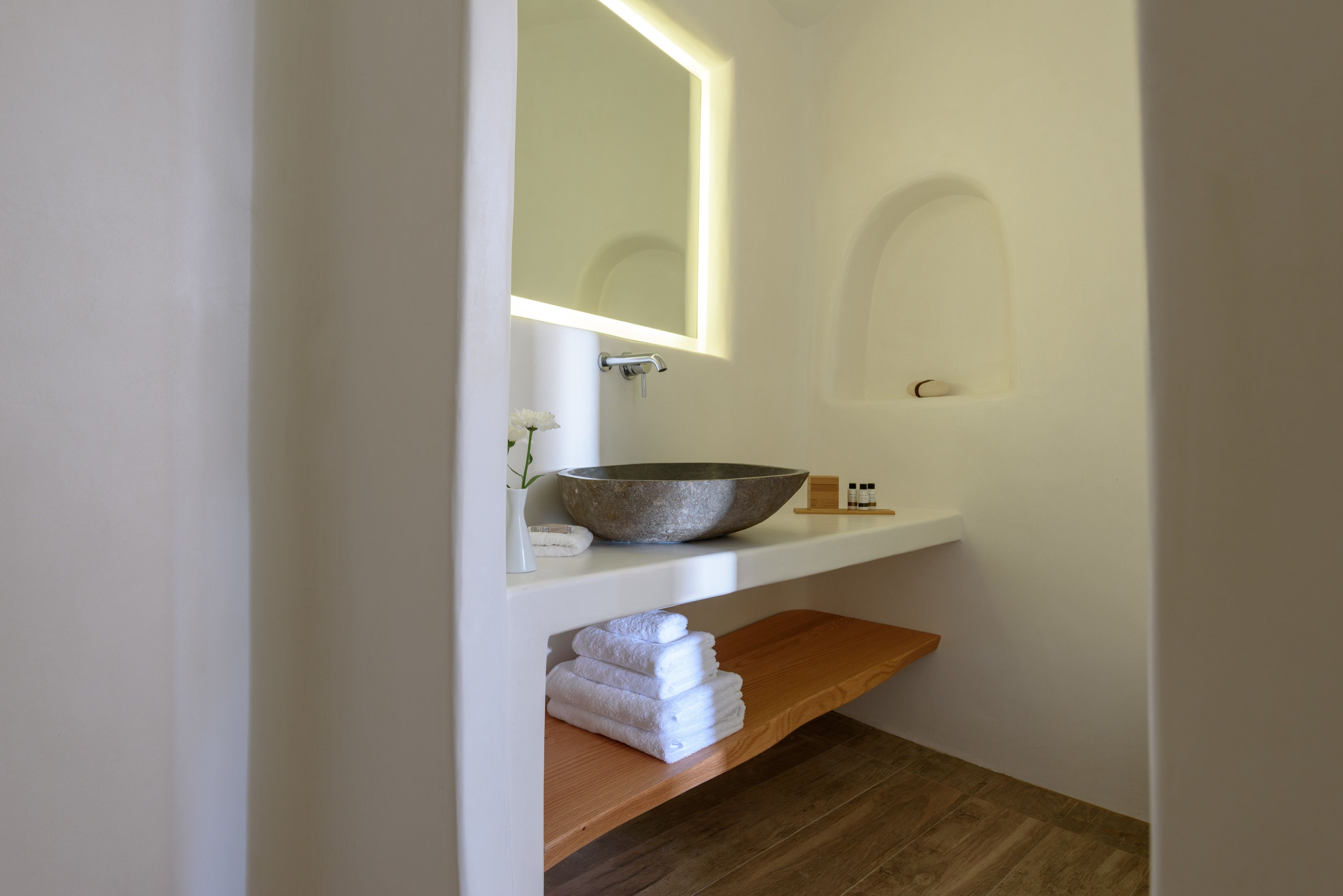 A bathroom with a large bowl sink, a mirror, and a wooden shelf with towels.