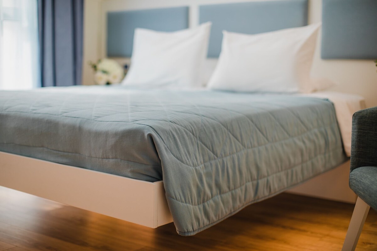 A bed with a grey quilt, white pillows, and a grey chair.