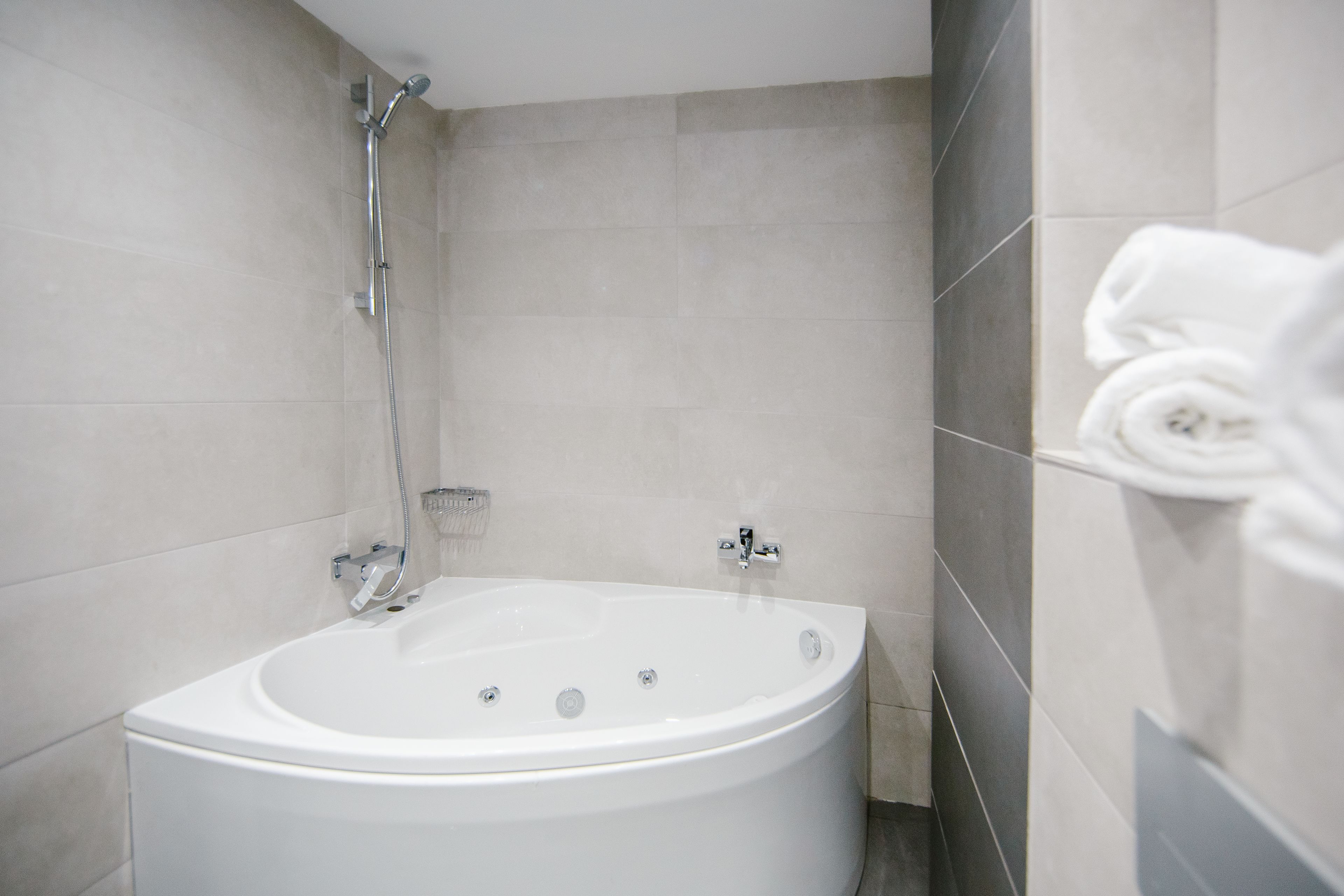 A modern bathroom with a freestanding bathtub, a handheld showerhead, and a towel rack with folded towels.