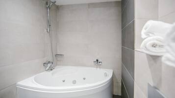 A modern bathroom with a freestanding bathtub, a handheld showerhead, and a towel rack with folded towels.