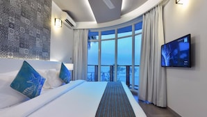 A modern hotel room with a large bed, a TV mounted on the wall, and a view of the ocean through large windows. - Velana Beach Hotel Maldives (Maafushi)