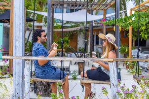 Una pareja sentada en un banco de madera colgante al aire libre, con una estructura de pérgola y follaje en el fondo.