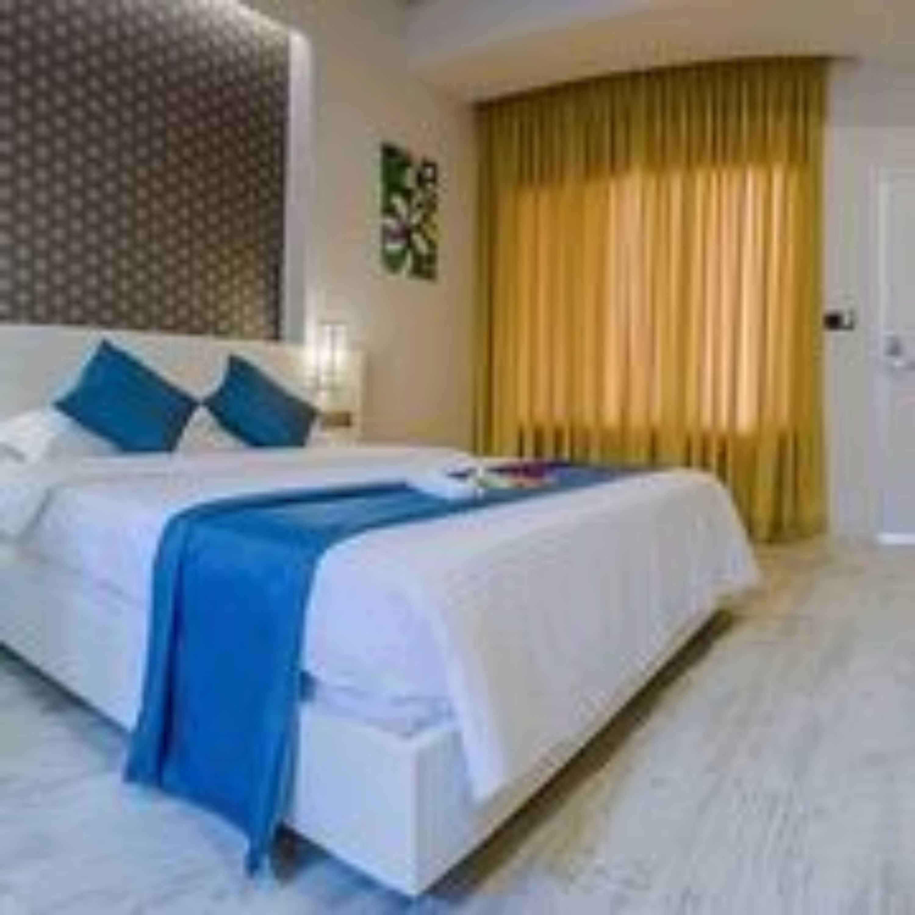 A hotel room with a bed, pillows, a nightstand, and a window with curtains.