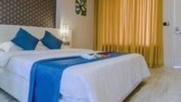 A hotel room with a bed, pillows, a nightstand, and a window with curtains.