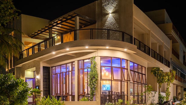 A modern hotel with a curved facade, large windows, and a balcony. - Velana Beach Hotel Maldives (Maafushi)