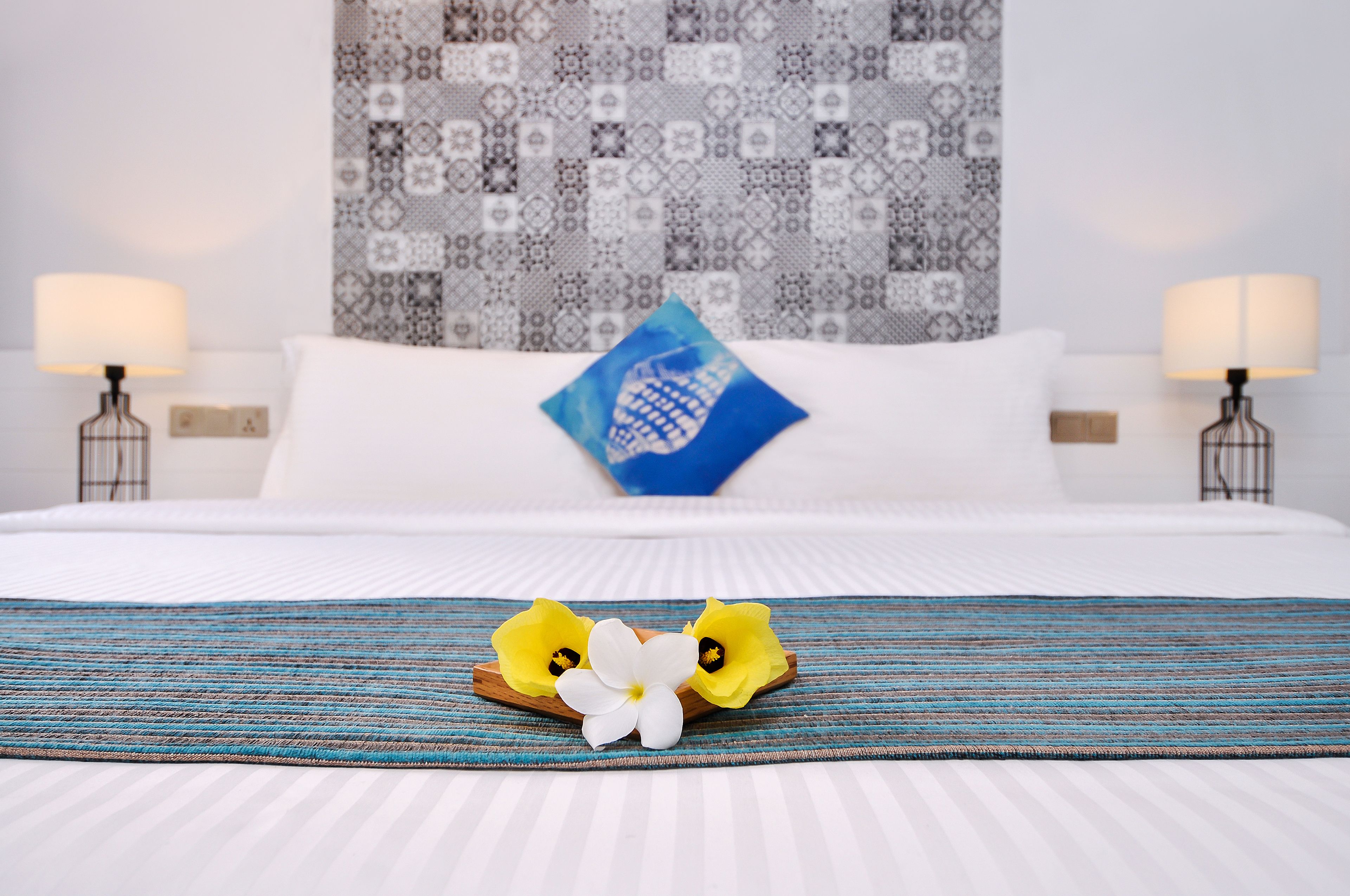 Una cama bien hecha con una colcha azul y blanca a rayas, un cojín decorativo y una mesita de noche con una lámpara.
