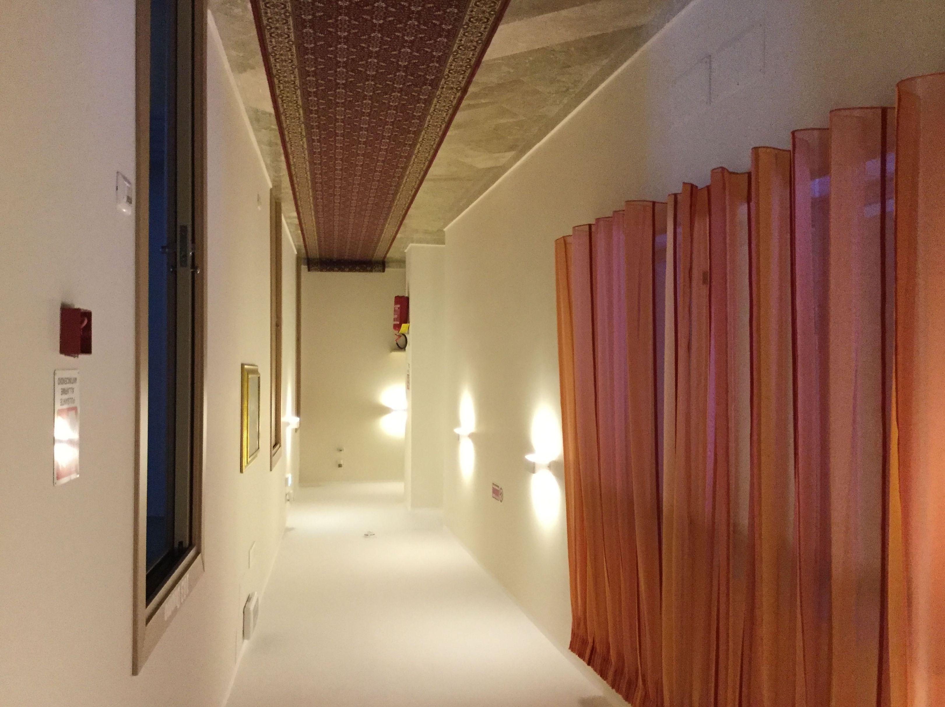 A hallway with a patterned ceiling, a wooden partition, and wall-mounted lights.