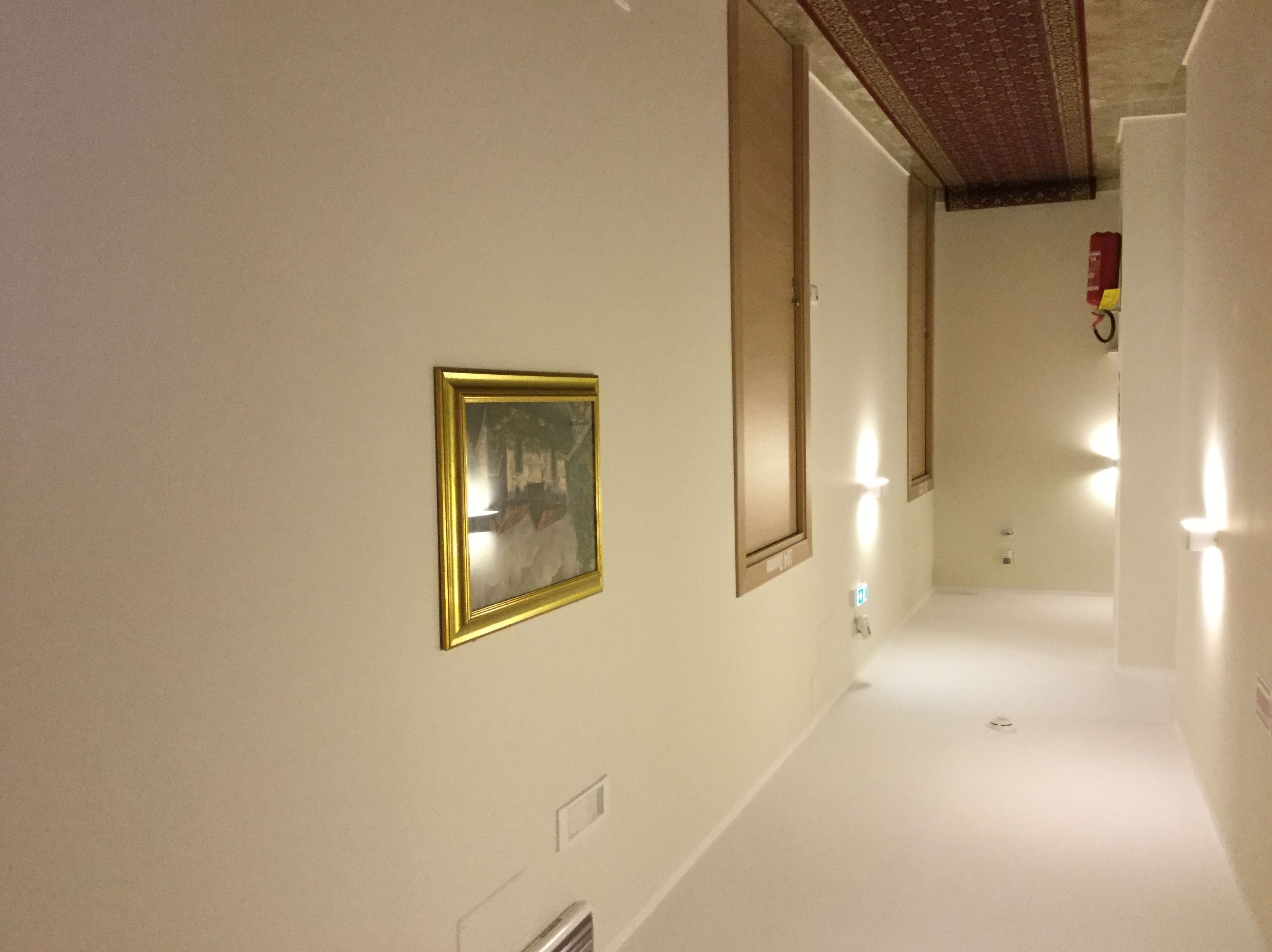 Ein Flur mit einem gerahmten Bild an der Wand, einem Lichtschalter und einem Rauchmelder.