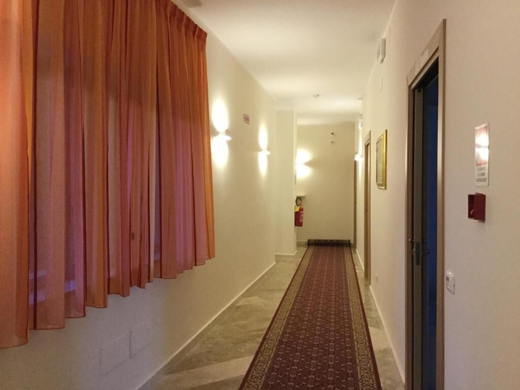 Pasillo de hotel con suelo alfombrado, un extintor y una puerta a la derecha.