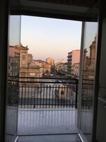Un balcón con vista a un paisaje urbano, que incluye edificios y una calle con gente caminando.
