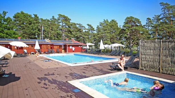 A pool area with two separate pools, lounge chairs, umbrellas, and a wooden deck. - Ljugarn Semesterby (Ljugarn)