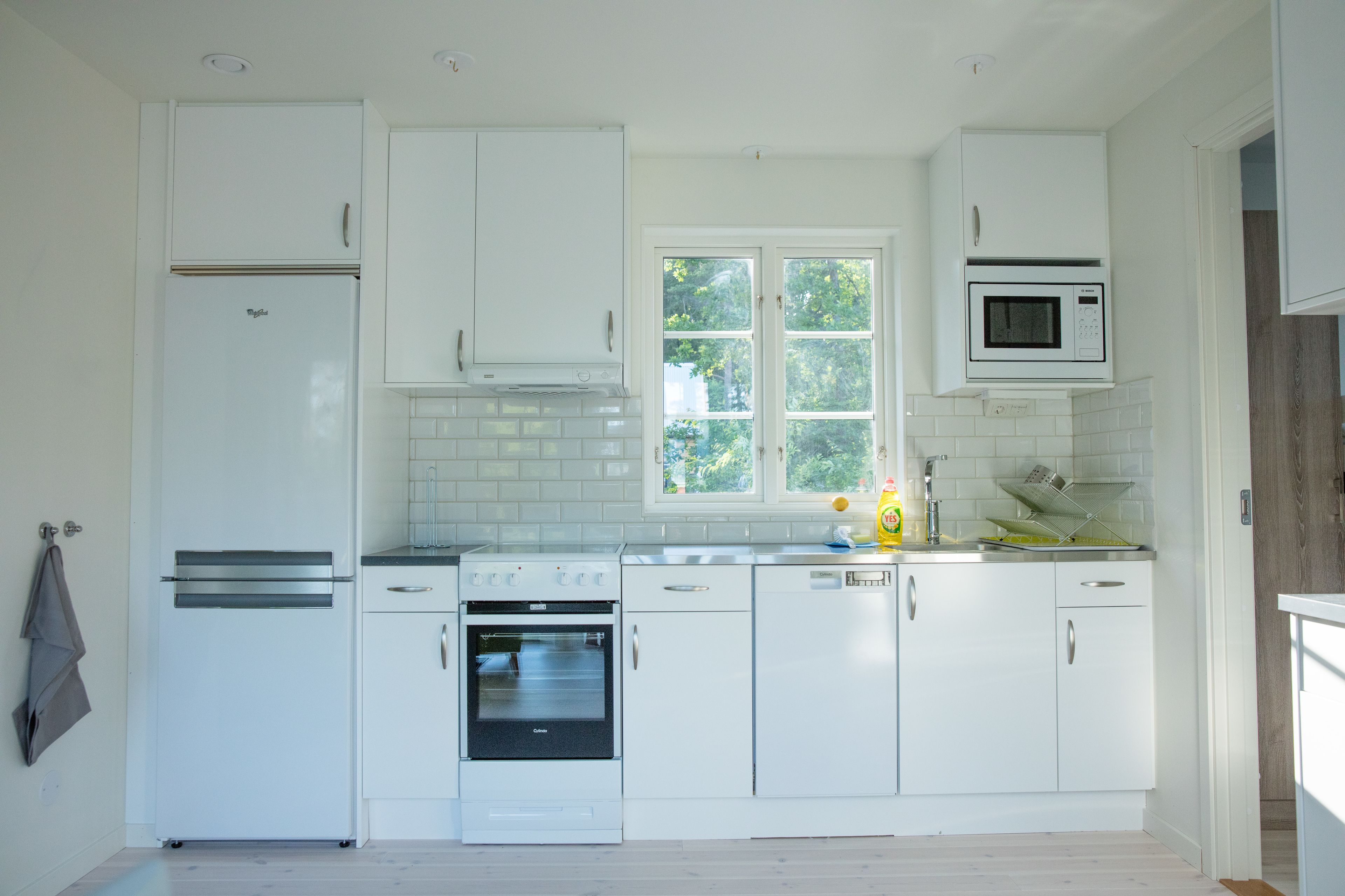 A modern kitchen with white cabinetry, a built-in oven, a microwave, and a window providing natural light.