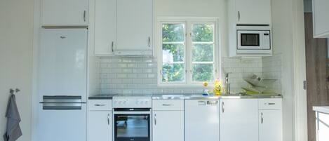 A modern kitchen with white cabinetry, a built-in oven, a microwave, and a window providing natural light.