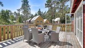 A wooden deck with wicker chairs and a table, overlooking a forested area with houses. - Ljugarn Semesterby (Ljugarn)