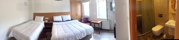 Quarto de hotel com duas camas de solteiro, uma mesinha, uma cadeira e banheiro com vaso sanitário e chuveiro.