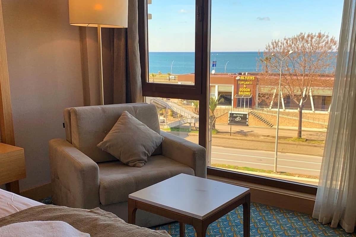 A hotel room with a large window offering a view of the beach and a sign for 'Alyans Toplanti'.