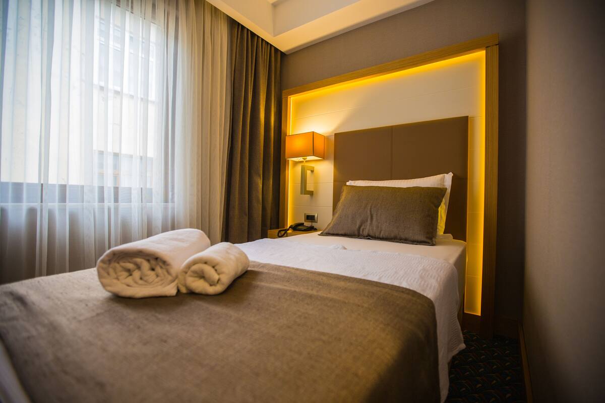 A hotel room with a neatly made bed, a bedside lamp, and a telephone on the nightstand.